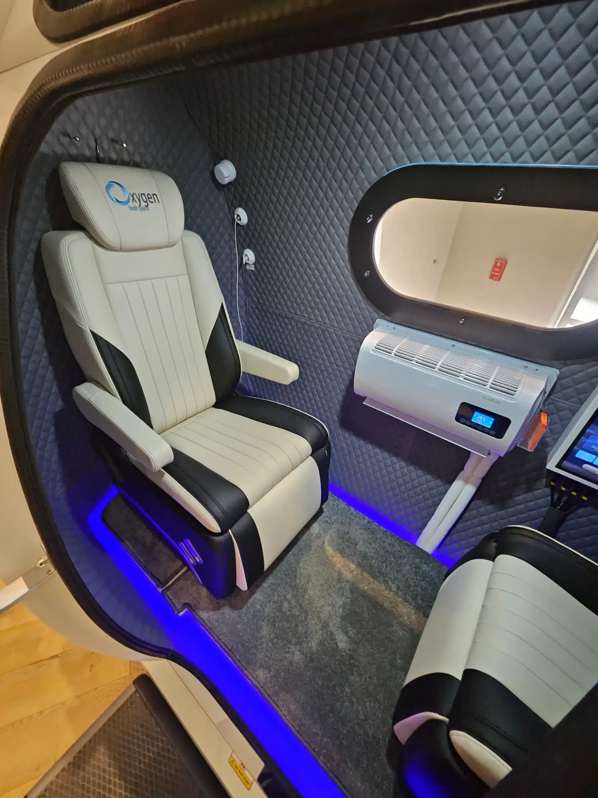 Quilted blue interior of a pod-style vehicle with cream leather seat, window, and blue LED floor lighting